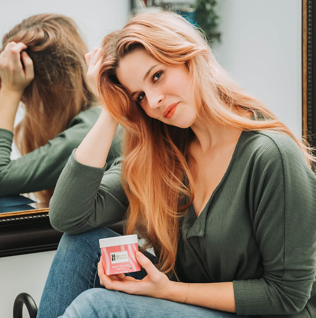 Woman holding Organic Essence Certified Organic Shea Cream Grapefruit jar sitting in front of mirror — clean organic daily moisturizer