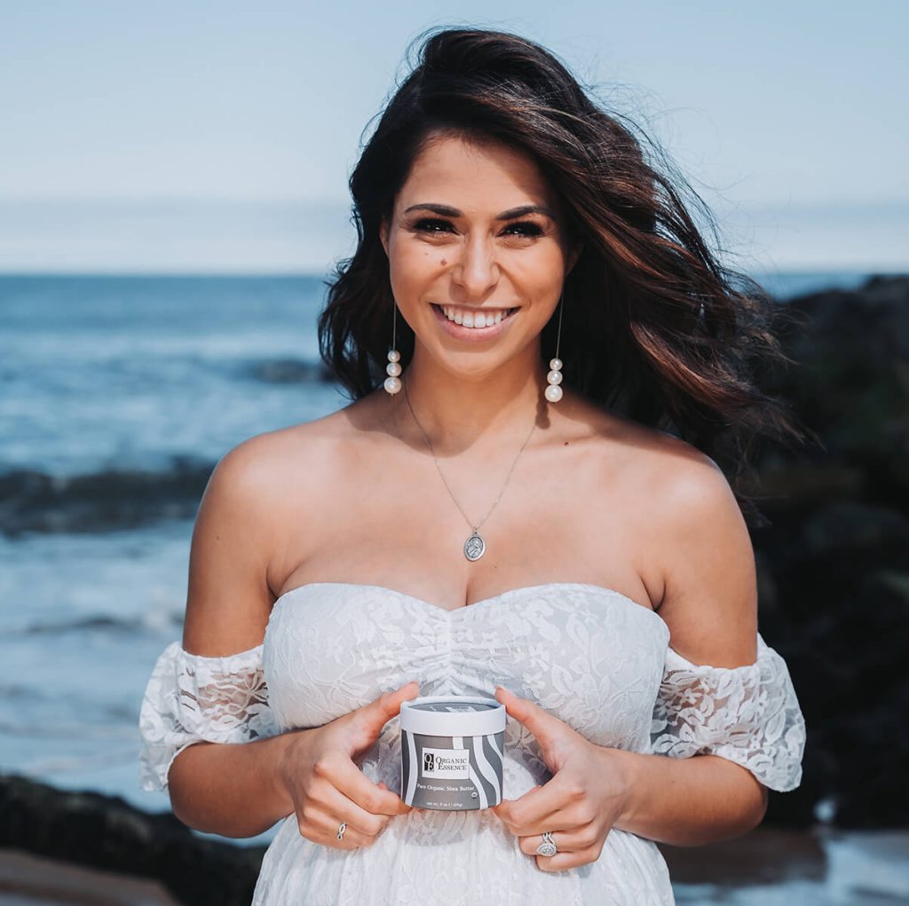 Pregnant woman holding Organic Essence pure organic shea butter jar beach lifestyle skincare