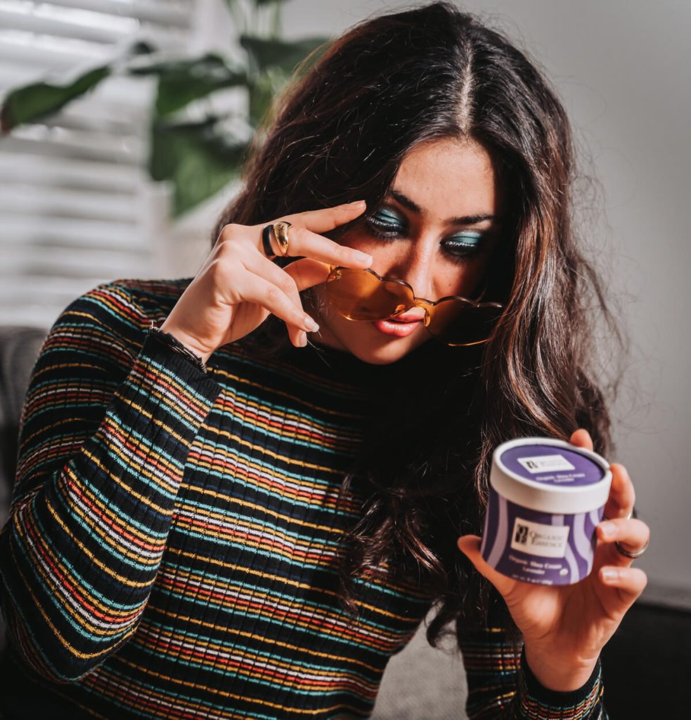 Woman holding Organic Essence certified organic shea cream lavender jar reviewing ingredient deck